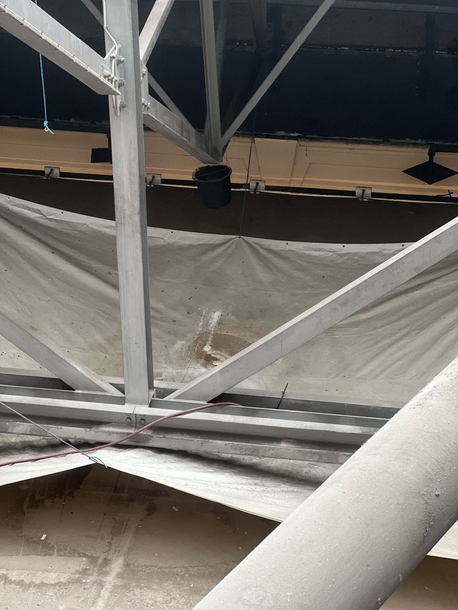 Inside the Alexandra Palace Great Hall: protective sheeting under the roof structure and a bucket catching water from the leak