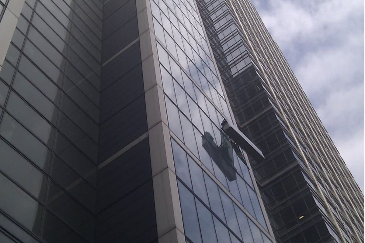 Looking up a glazed curtain wall office tower, with an operative working on the glazing at height