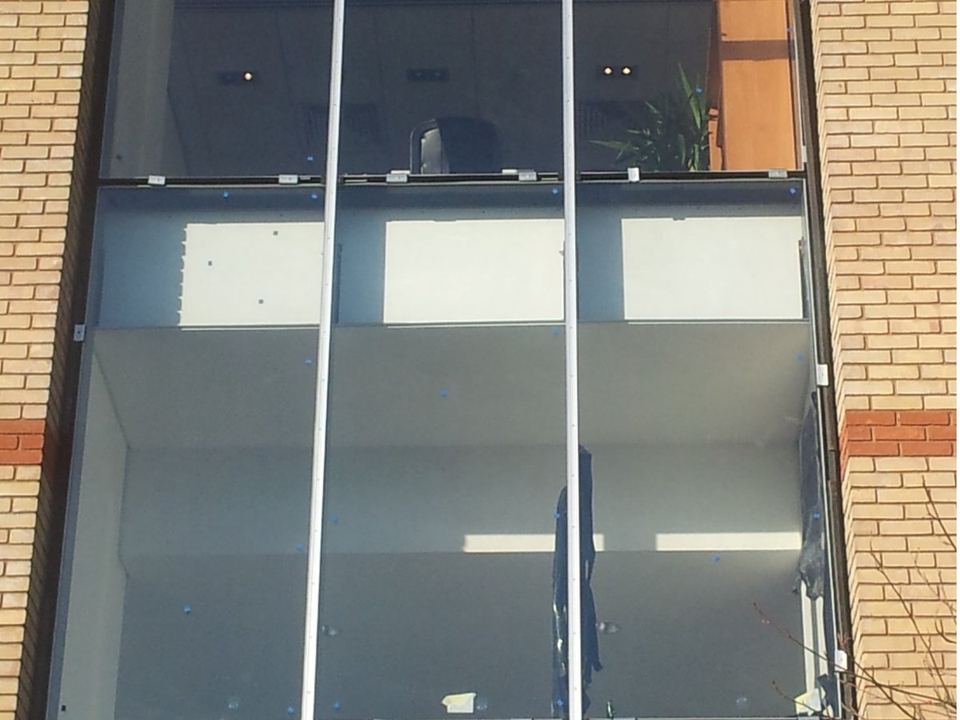 Aluminium-framed glazed screen set into a brick elevation, showing the mullion and transom joints where gaskets seal the glass
