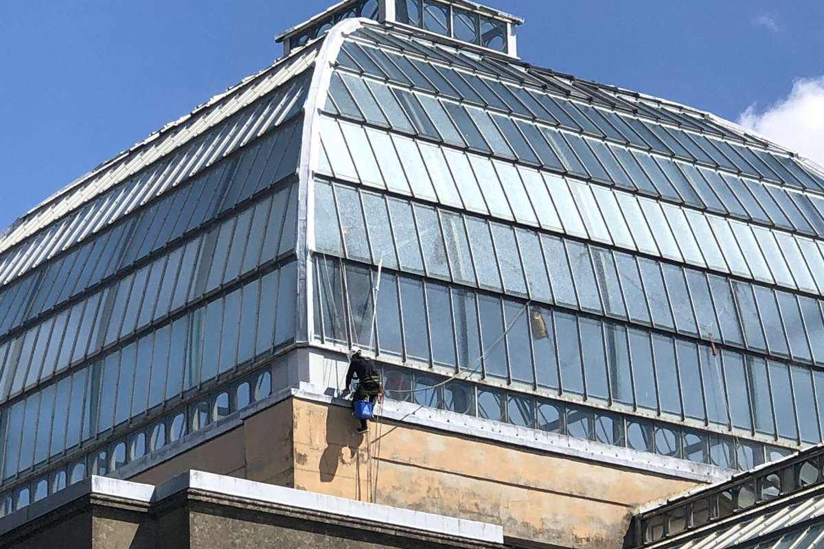 Rope-access technician with a blue bucket working at the base of a single glazed Victorian heritage glass roof dome on a Grade II listed building